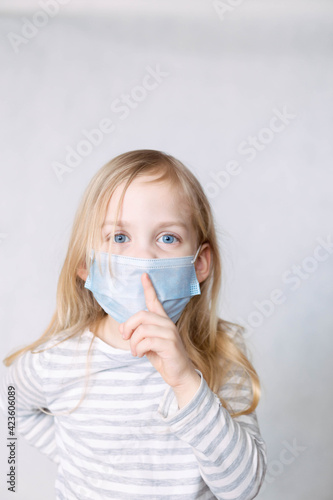 Blonde girl in striped blouse and medical mask removes the index finger to her lips © aleksa_photo_waw