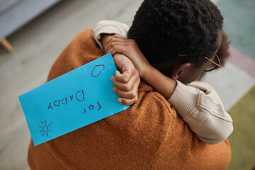Close up of happy father embracing little girl after coming home from work on Fathers day, focus on child holding letter for dad, copy space