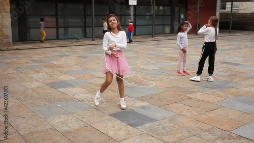 Cheerful sporty tween girl jumping rope in school yard during recess in warm autumn day. High quality FullHD footage