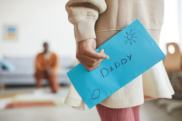 Close up of unrecognizable girl holding letter for dad while presenting handmade gift for Fathers day, copy space