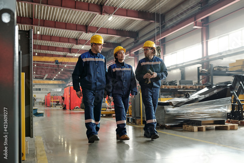 Group of workers or engineers of contemporary industrial plant moving along large workshop with equipment and having conversation