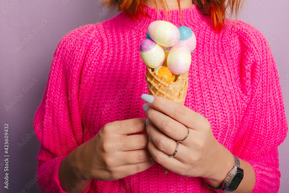 Female hand holding colorful ice cream made with chocolate eggs. Easter. Lilac background. - obrazy, fototapety, plakaty 