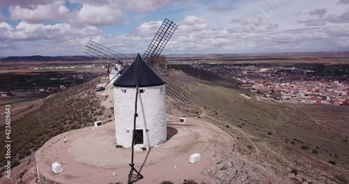 Aerial view of white cylindrical towers and pointed roofs of old Spanish windmills on background with Consuegra cityscape