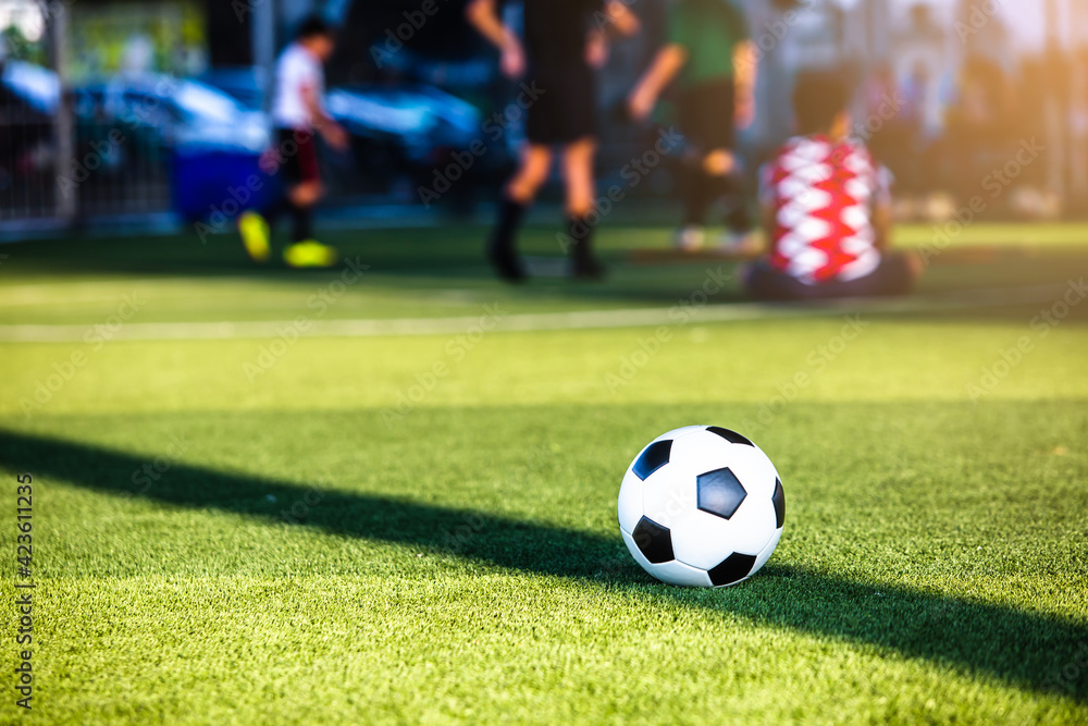 Selective focus to soccer ball on green artificial turf with blurry soccer team is training. Sport background. Soccer background. Selective focus to soccer ball on green artificial turf with blurry soccer team is training. Sport background. Soccer background.