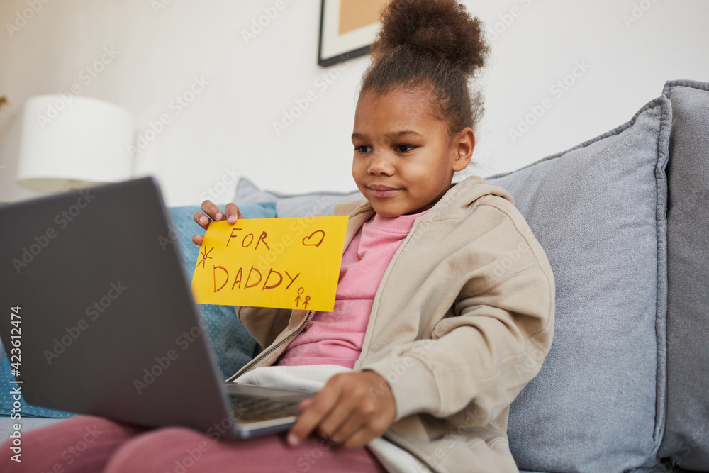 Portrait of cute African-American girl showing handmade card while talking to dad via video chat and social distancing, copy space Portrait of cute African-American girl showing handmade card while talking to dad via video chat and social distancing, copy space