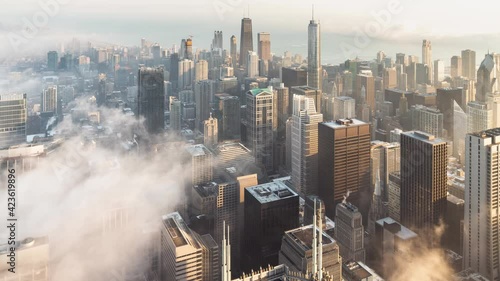Incredible panning up aerial skyline time lapse as patches of dense low fog makes its way into the heart of downtown Chicago and over Lake Michigan surrounding the highrise buildings at sunrise.
