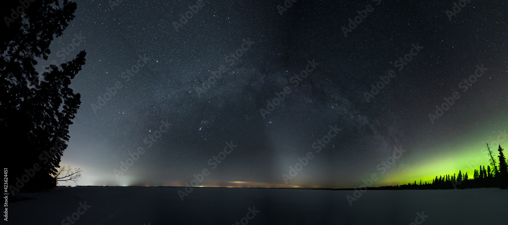 Panoramic view of a star filled night sky with the Milky Way and some Aurora above a snow covered lake.  The Zodiacal light can also be seen on the horizon.
