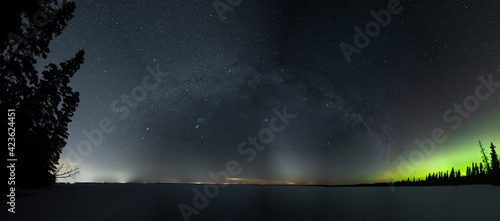 Panoramic view of a star filled night sky with the Milky Way and some Aurora above a snow covered lake. The Zodiacal light can also be seen on the horizon. 