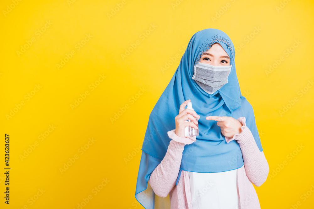 Asian Muslim Arab woman Islam wear veil hijab and face mask protect point alcohol spray to hands isolated yellow background Asian Muslim Arab woman Islam wear veil hijab and face mask protect point alcohol spray to hands isolated yellow background