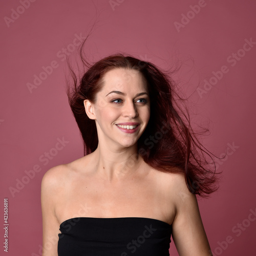 Close up portrait of a red haired woman with expressive facial features on a pink studio background.