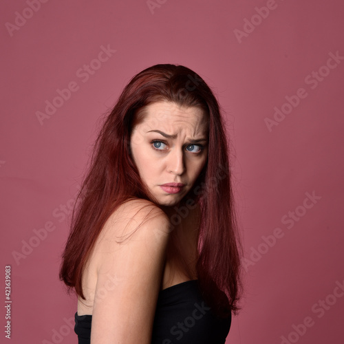 Close up portrait of a red haired woman with expressive facial features on a pink studio background.