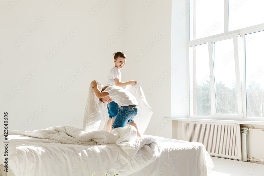 Indoor positive activity. Small children jumping on a bed and having fun fighting with pillows in sunshine Indoor positive activity. Small children jumping on a bed and having fun fighting with pillows in sunshine