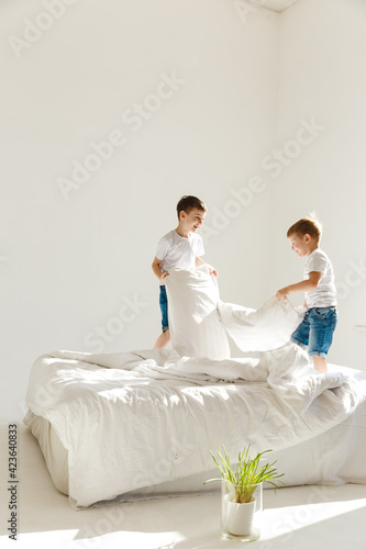 Indoor positive activity. Small children jumping on a bed and having fun fighting with pillows in sunshine