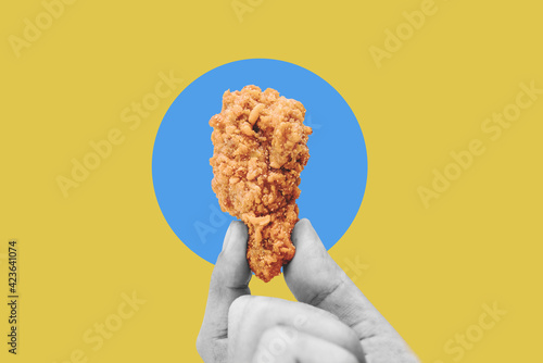 Hand holding fries chicken drumstick, on blue yellow background photo