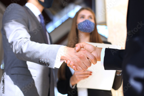 Business people in protective masks shaking hands, finishing up a meeting.