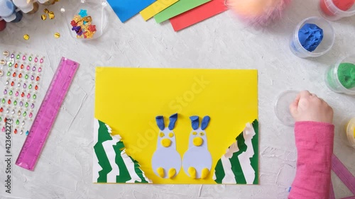 Child making card with Easter bunnies toys from colorful paper and placticine. Handmade. Project of children's creativity, handicrafts, crafts for kids. photo