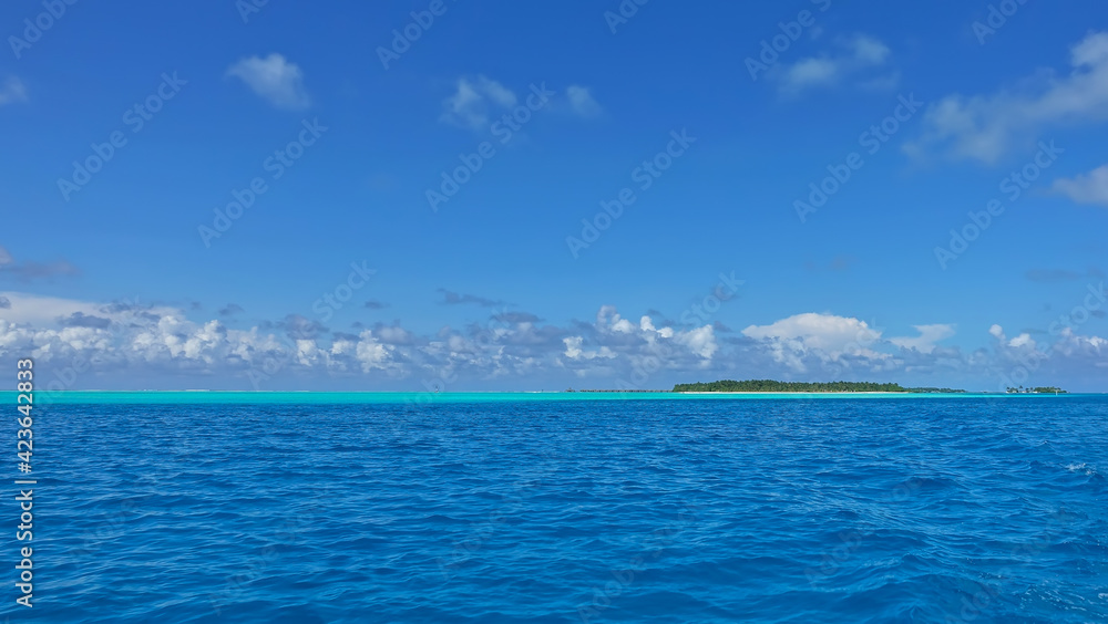 Calm turquoise and aquamarine ocean. Azure sky with picturesque clouds. An island with tropical vegetation is visible in the distance. Maldives. Endless summer Calm turquoise and aquamarine ocean. Azure sky with picturesque clouds. An island with tropical vegetation is visible in the distance. Maldives. Endless summer