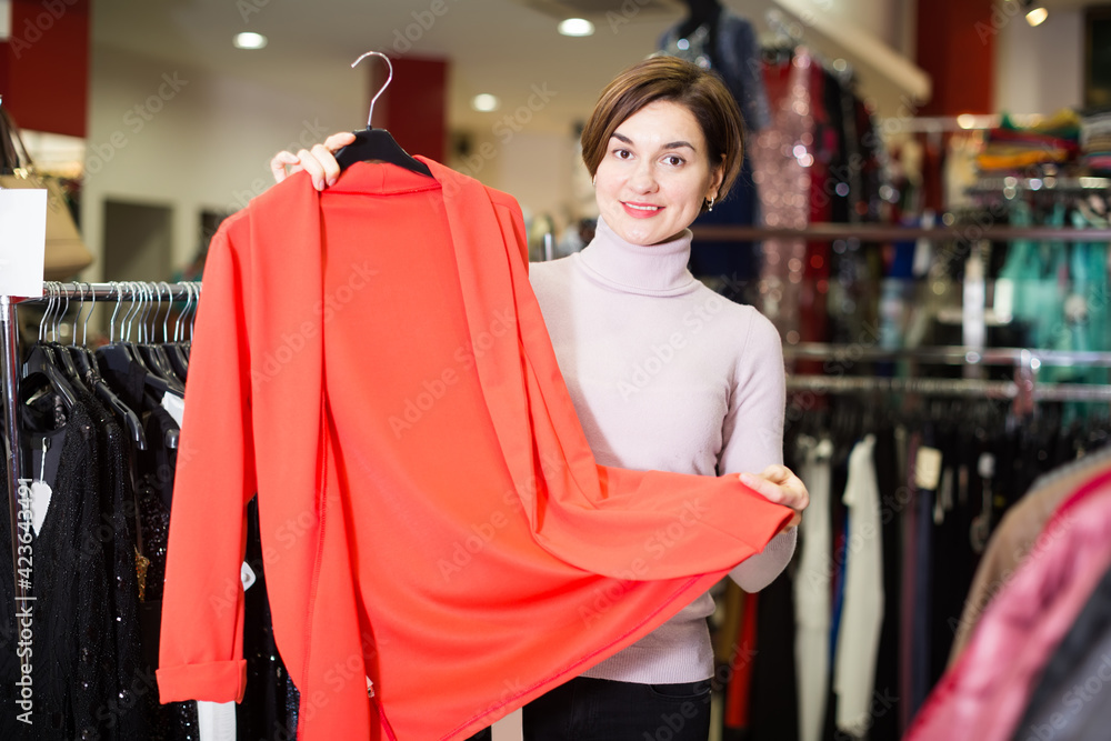 Smiling woman shows a stylish jacket in the women's clothing store