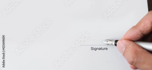 Hand holds pen and signs agreement contract on the table.