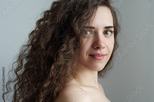 Portrait of a beautiful young lady with long curly brown hair and expressive green eyes. Curly hair care. Caring for the skin. The model is posing for the camera. Natural beauty concept