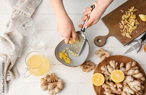 Woman grating ginger on white wooden background photo