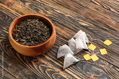 Tea bags and bowl with dry leaves on wooden background