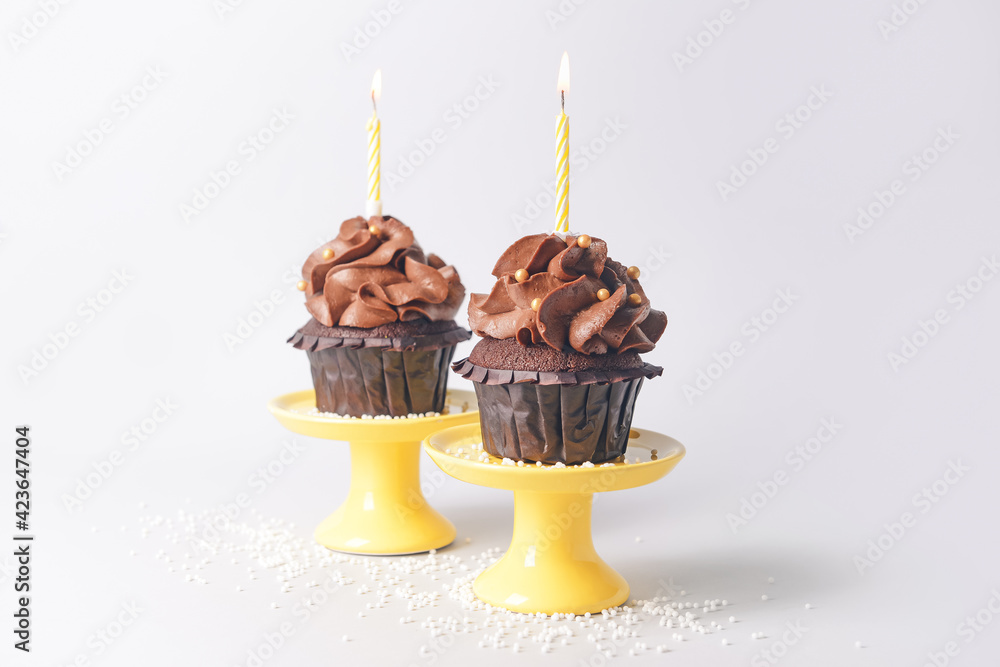 Tasty chocolate cupcakes with candles on light background - obrazy, fototapety, plakaty 
