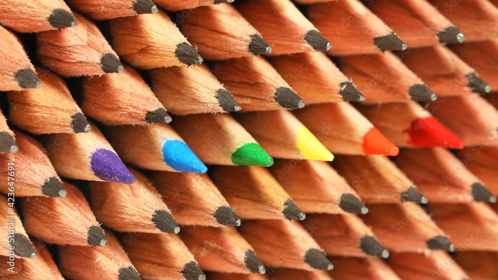 The gay and lesbian rainbow LGBT flag. Symbolic colors of purple blue green yellow orange red arranged with sharp colored pencils in amongst rows of boring plain normal graphite pencils