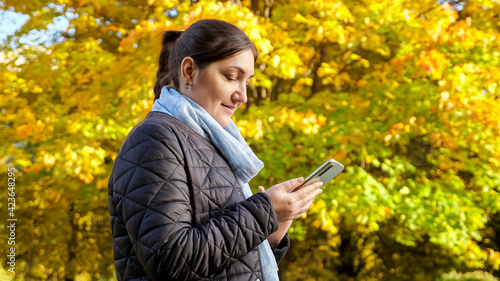 Young woman with phone on background of yellow trees.