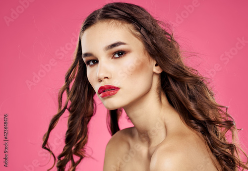Sexy brunette with loose hair on a pink background with bright makeup