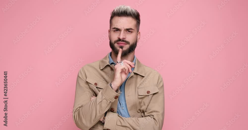 sexy unshaved guy looking to side, wearing beige jacket and crossing arms, smiling and making warning gesture, turning around and leaving on pink background in studio sexy unshaved guy looking to side, wearing beige jacket and crossing arms, smiling and making warning gesture, turning around and leaving on pink background in studio