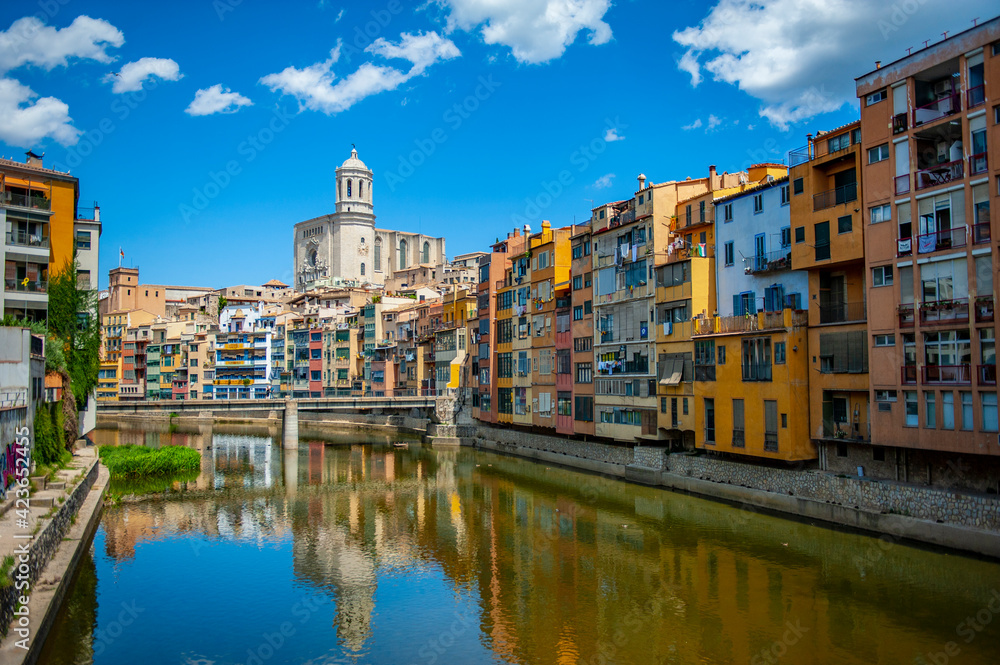 Girona, Spain - July 28, 2019: Beautiful colorful riverside houses in the Jewish quarter of Girona city in Catalunya, Spain, with Girona Cathedral in the background