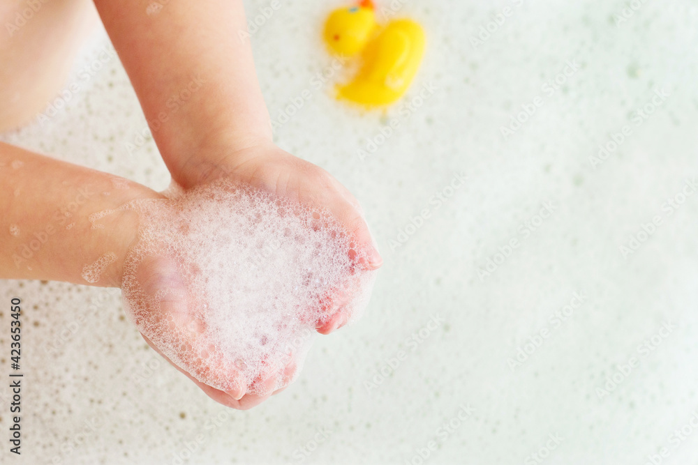 Fototapeta premium little baby girl playing with foam in a bath tub. Child playing with a toys in the bathroom.