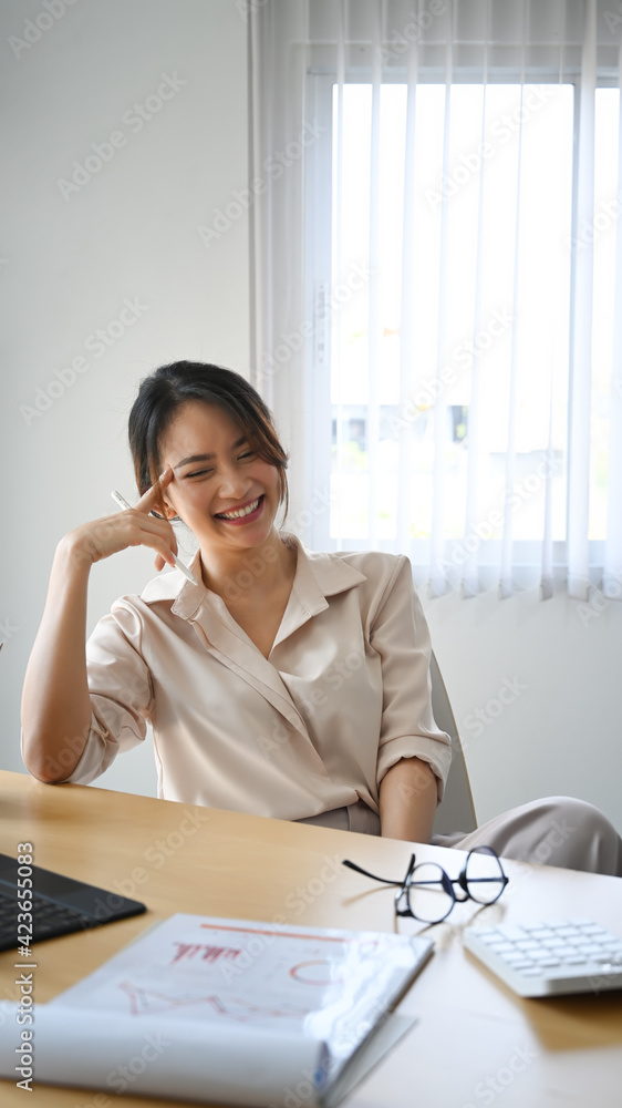 Portrait of happy female accountant sitting at her workplace and laughing. Portrait of happy female accountant sitting at her workplace and laughing.
