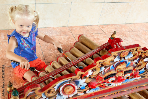 Little funny child play music on traditional indonesian musical instrument - bamboo xylophone Rindik or Tingklik. Arts, culture of Bali island and Indonesia. photo