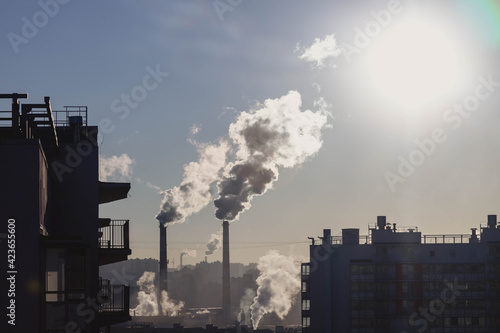 Landscape emission to atmosphere from industrial pipes. Smokestack at sunrise in residential block of apartment building. Steam or smoke heat and power plant in city. Global warming and air pollution