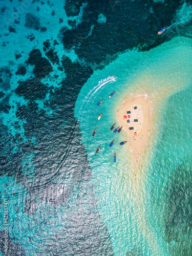 View from above or from a bird's eye view of the coral island, the white sand beach and the beautiful, clear turquoise waves with boats.