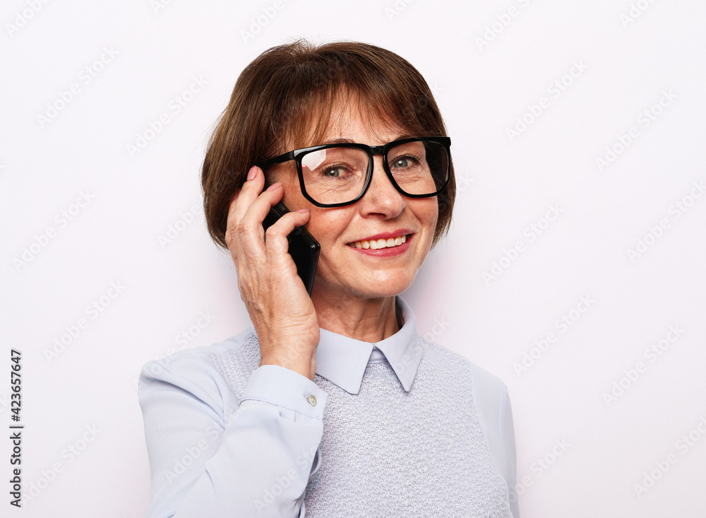 Happy senior woman using mobile phone over white background. Beautiful stylish elderly lady talking on cellphone.