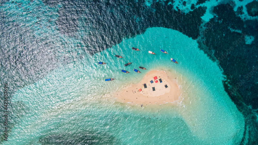 View from above or from a bird's eye view of the coral island, the white sand beach and the beautiful, clear turquoise waves with boats.