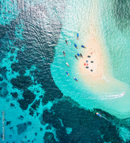 View from above or from a bird's eye view of the coral island, the white sand beach and the beautiful, clear turquoise waves with boats.