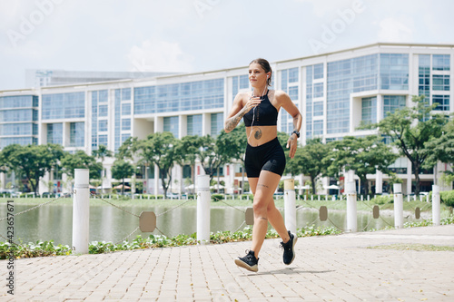 Fit positive young woman training for racewalking competition, she is listening to music when walking around small pond