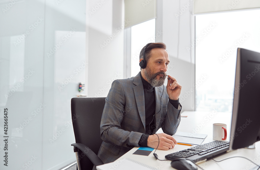 Happy matured man with headphones is sitting in a light white office Happy matured man with headphones is sitting in a light white office