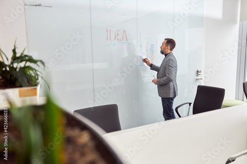 Caucasian adult man in office is writing on the glass desk