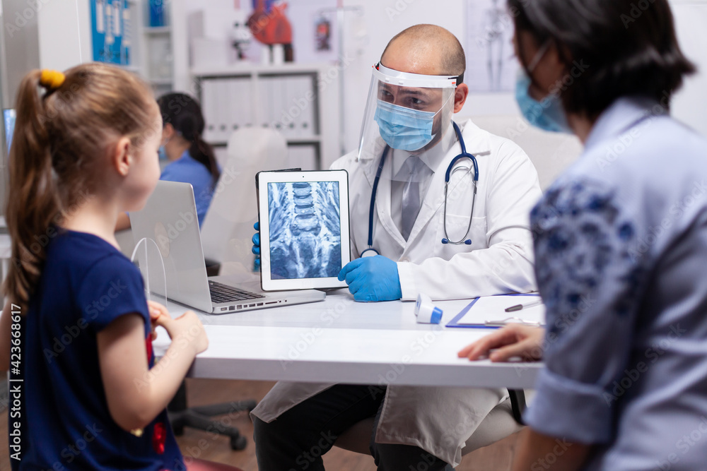 Specialist doctor showing medical report to mother and daughter on a digital tablet in hospital. Specialist talking about medical examination for infections, disease providing healtcare services Specialist doctor showing medical report to mother and daughter on a digital tablet in hospital. Specialist talking about medical examination for infections, disease providing healtcare services