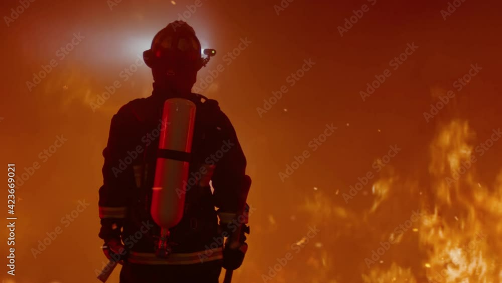 Dramatic silhouette of American firefighter in full gear exploring the huge fire zone. Shot with 2x anamorphic lens Dramatic silhouette of American firefighter in full gear exploring the huge fire zone. Shot with 2x anamorphic lens