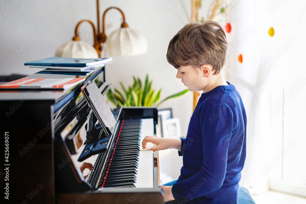 Beautiful little kid boy playing piano in living room. Child having fun  with learning to play music instrument with tablet app. E-learning concept  during homeschooling corona virus lockdown. Stock Photo | Adobe