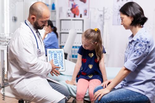 Tableau sur toile Specialist doctor holding tablet with radiography during medical examination of child in hospital office