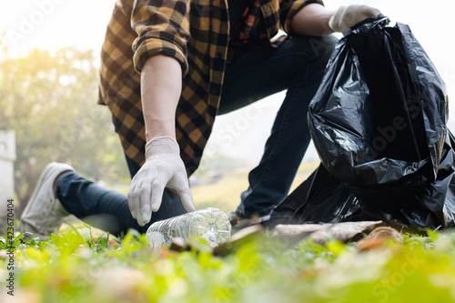 Man's hands pick up plastic bottles, put garbage in black garbage bags to clean up at parks, avoid pollution, be friendly to the environment and ecosystem