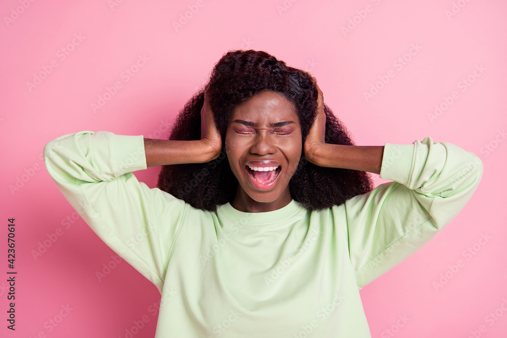 Photo of unhappy sad dark skin young woman hold hands head cover ears isolated on pastel pink color background Photo of unhappy sad dark skin young woman hold hands head cover ears isolated on pastel pink color background