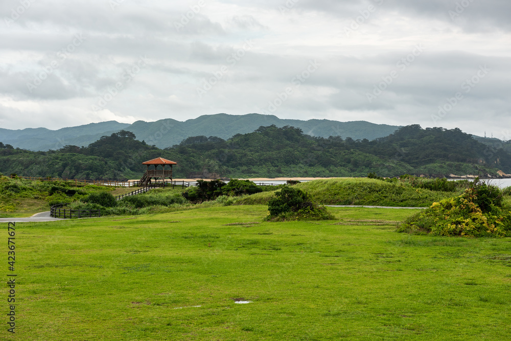 Park with green vegetation, a lookout view point to contemplate the beautiful landscape and mountains in the background on a cloudy day. Iriomote Island.